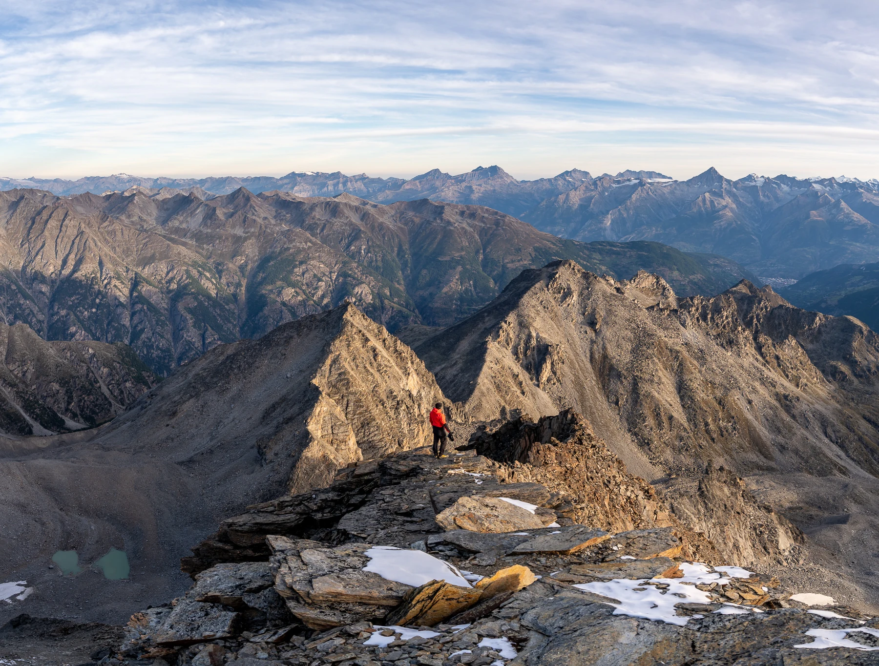 Kevin Buess — Landschaftsfotograf auf felsigem Bergkamm mit weitem Walliser Alpenpanorama bei Morgenlicht, Schweiz