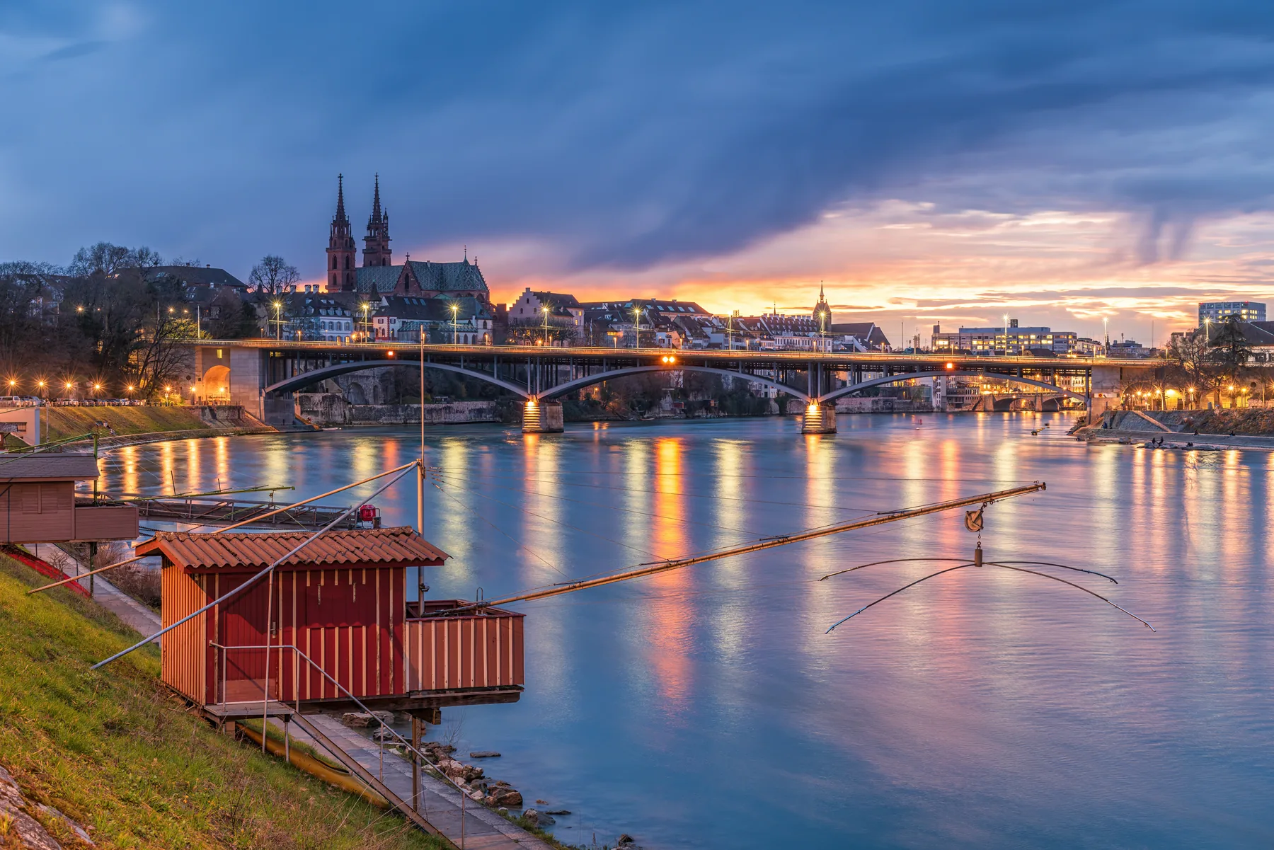 Basel Stadtpanorama bei Sonnenuntergang: Rhein mit Spiegelungen, Mittlere Brücke und Basler Münster im Abendrot