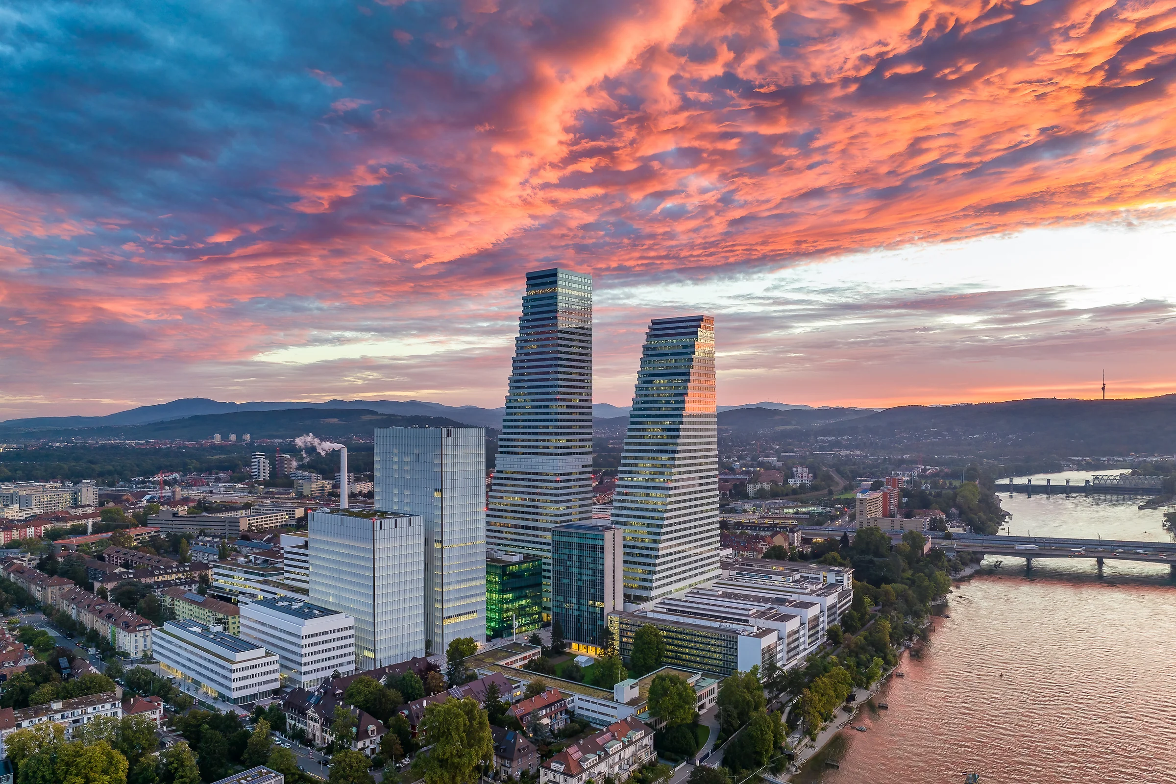 Luftaufnahme der Roche Türme in Basel bei dramatischem Sonnenuntergang mit leuchtendem Abendhimmel am Rhein