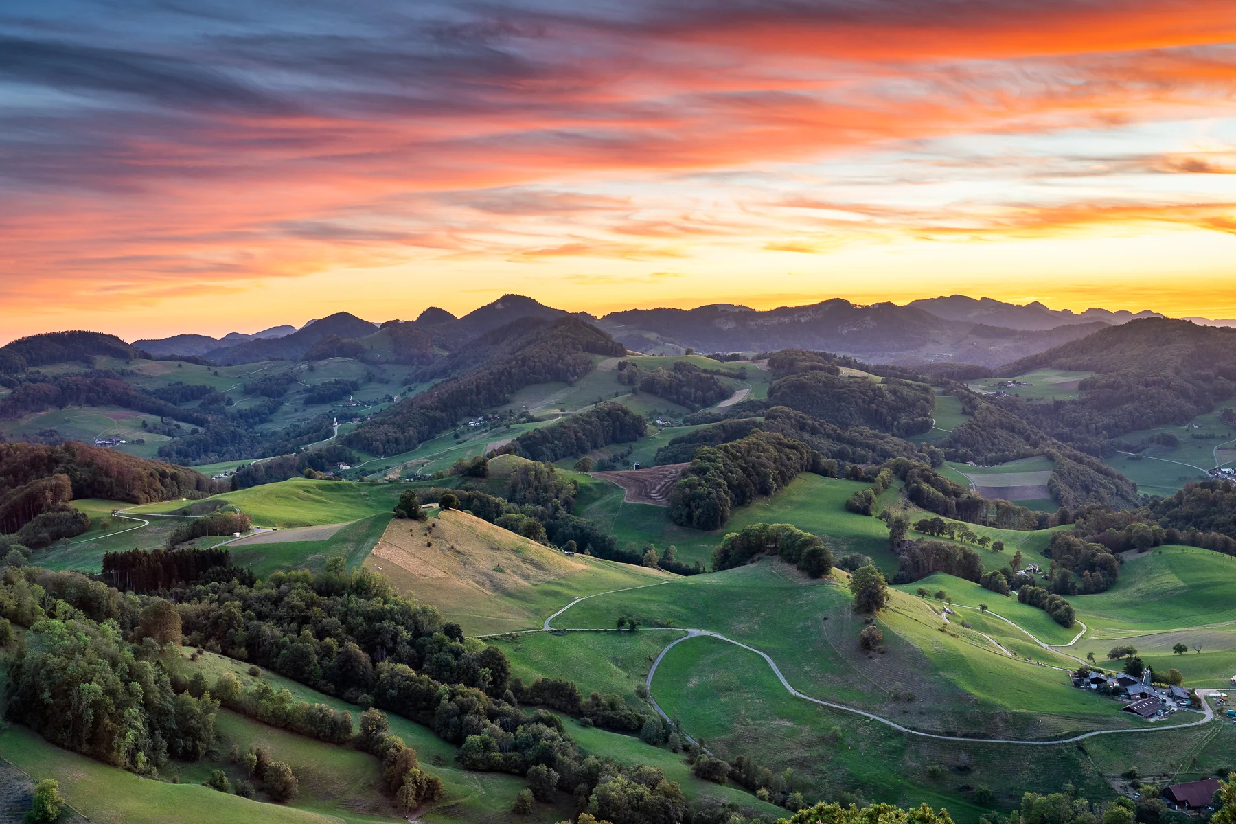 Goldener Sonnenuntergang über Baselland mit dramatischen Wolken, grünen Wiesen und dichten Wäldern in der Berglandschaft