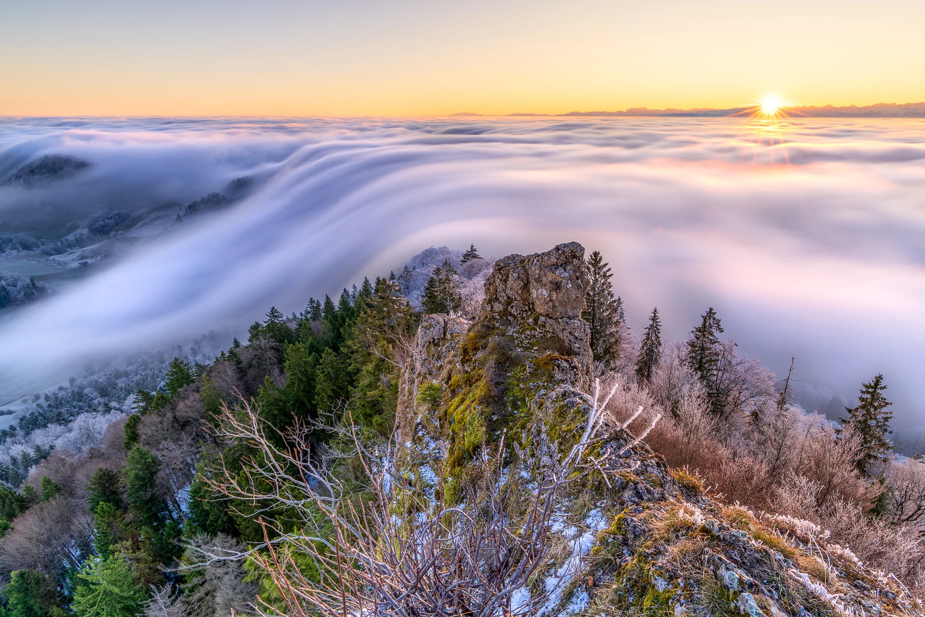 Dramatischer Sonnenaufgang über einer Nebelwelle in Baselland mit Alpengipfeln und Waldlandschaft