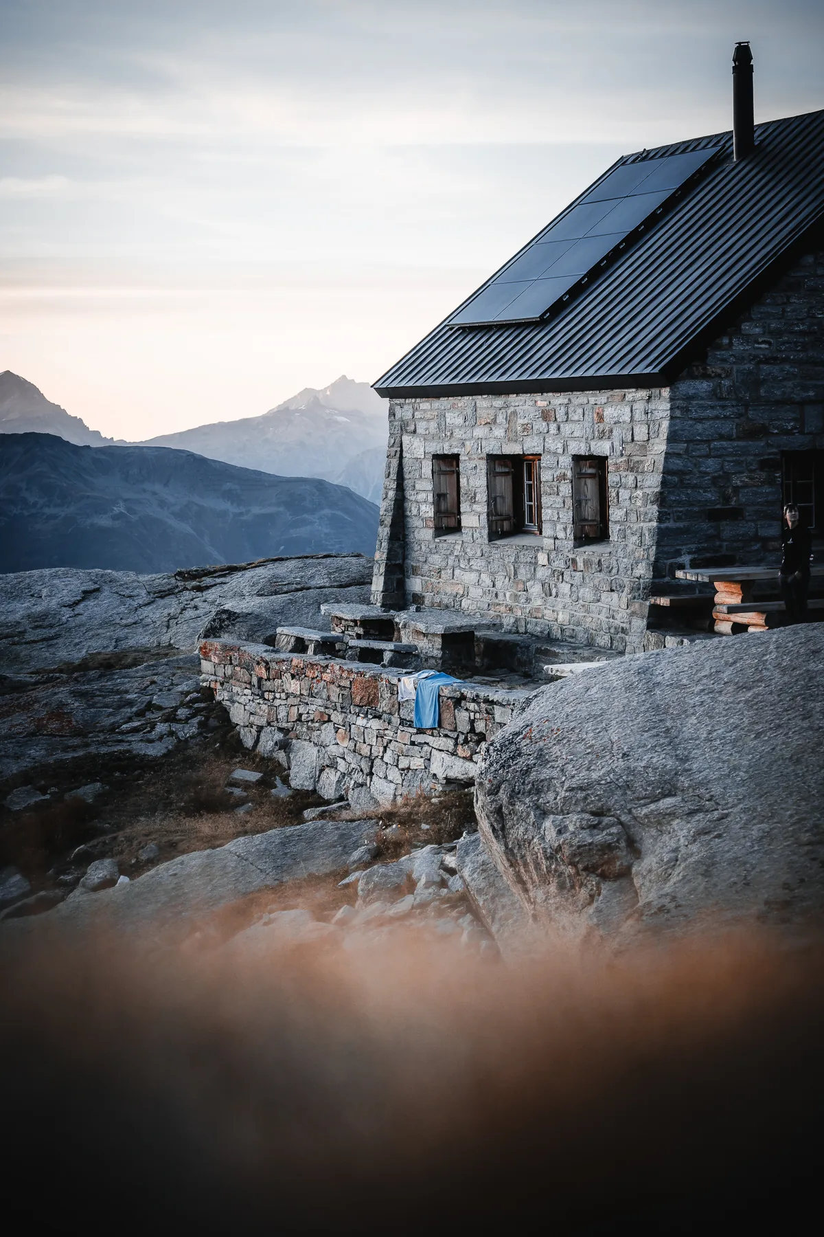 Rustikale Steinberghütte mit Solarpanelen auf Metalldach, felsige Alpenlandschaft bei Abenddämmerung, Bordierhütte SAC, Wallis, Schweiz