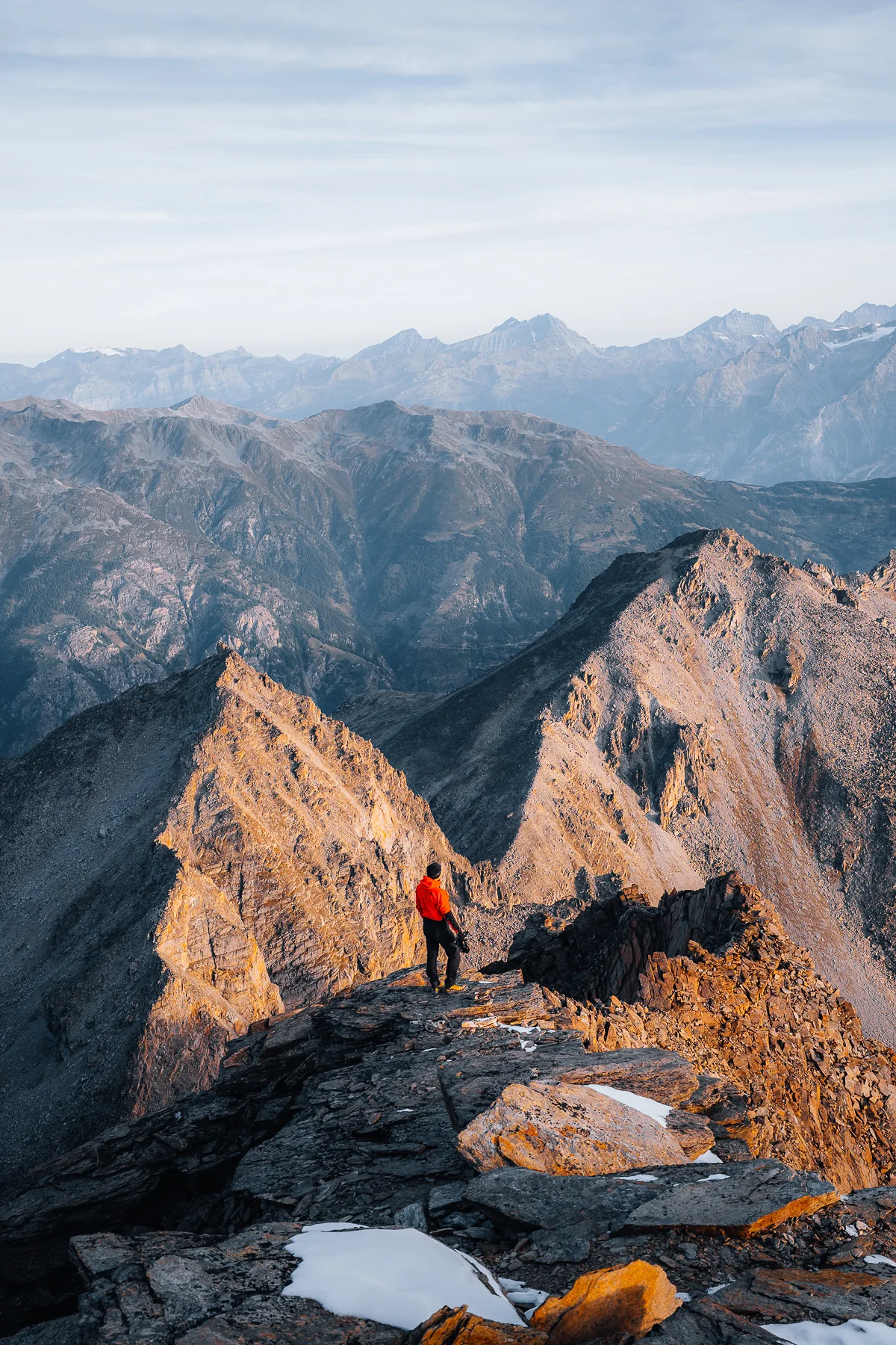 Bergsteiger in roter Jacke auf Felsengrat mit Alpenglühen und weitem Bergpanorama, Gross Bigerhorn, Wallis, Schweiz
