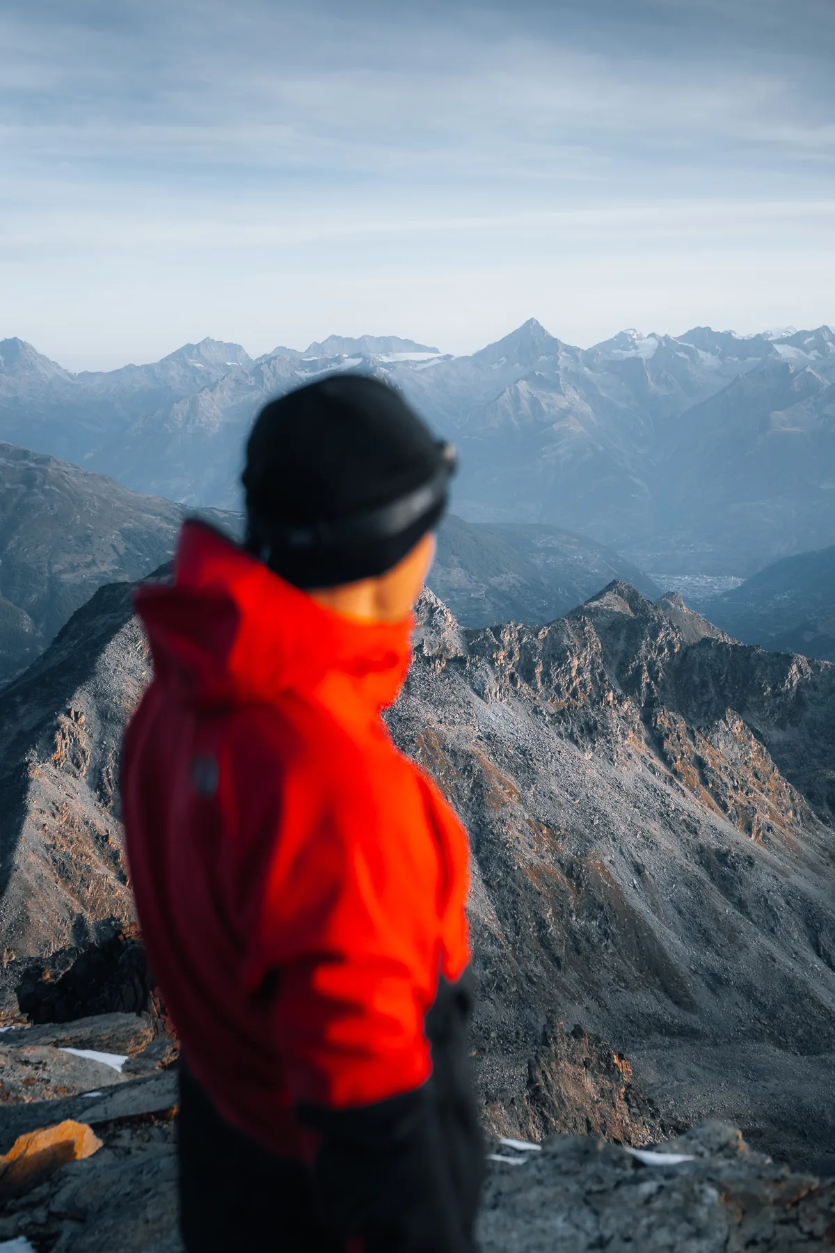 Bergsteiger in roter Jacke steht auf Berggipfel und blickt auf Gross Bigerhorn, Wallis, Schweiz
