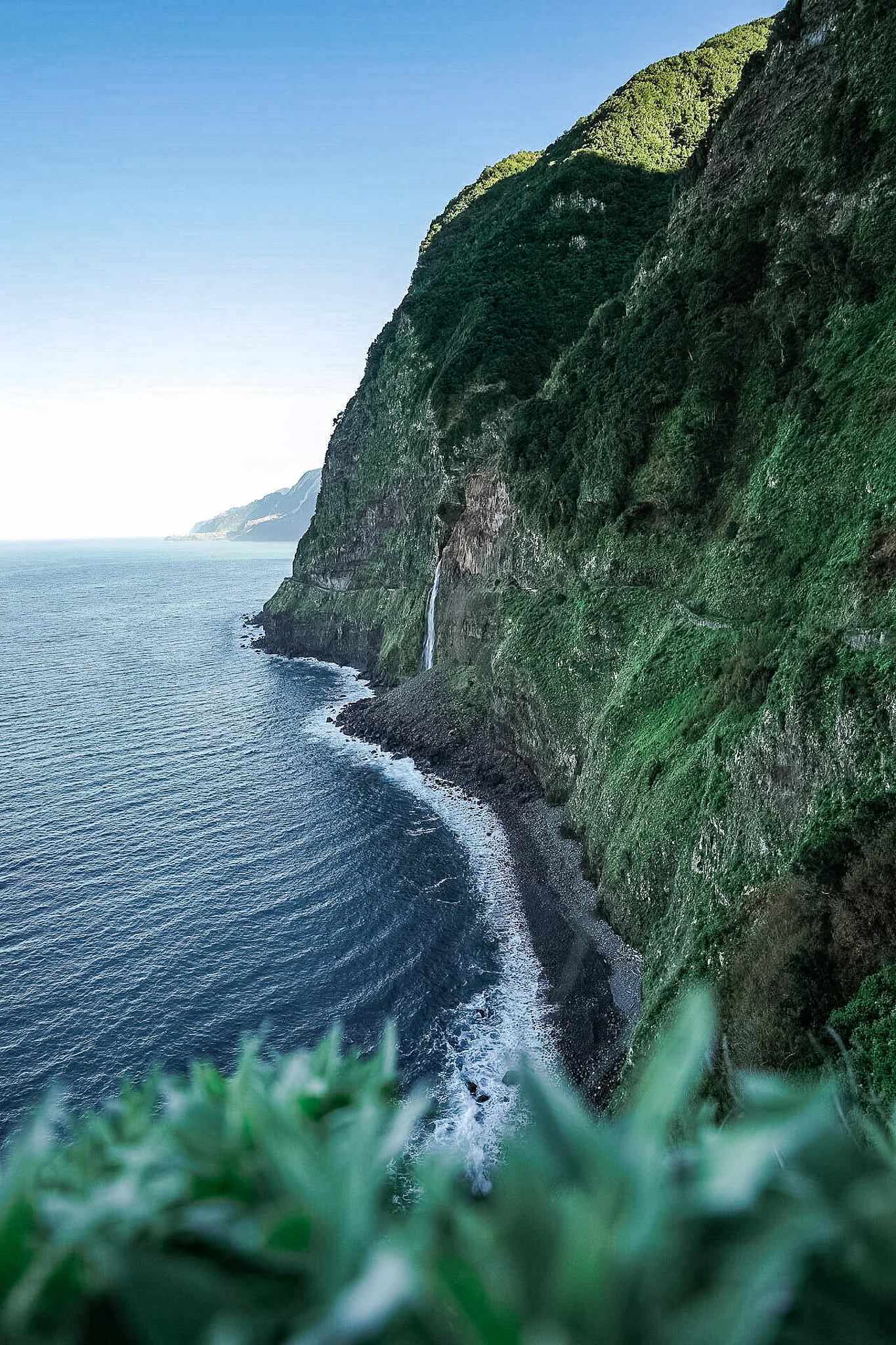 Steile grüne Küstenklippen Madeiras mit Wasserfall der direkt in den Atlantik stürzt, Nordküste Portugal