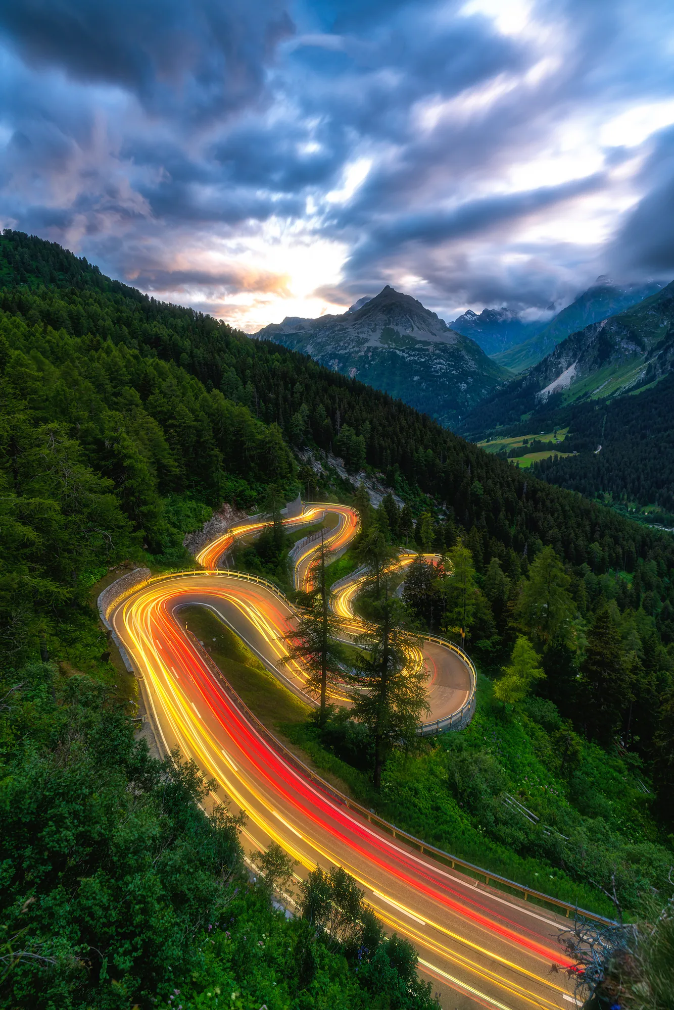 Lichtspuren auf kurvenreicher Passstrasse in den Alpen bei Abenddämmerung, Langzeitbelichtung Graubünden Schweiz