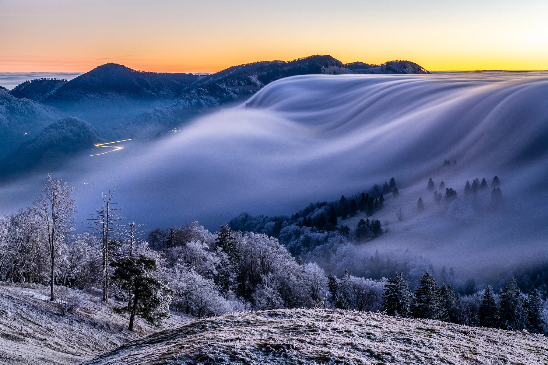 Dramatische Nebelwelle über dem Scheltenpass bei Sonnenaufgang mit verschneiten Wäldern und Berggipfeln