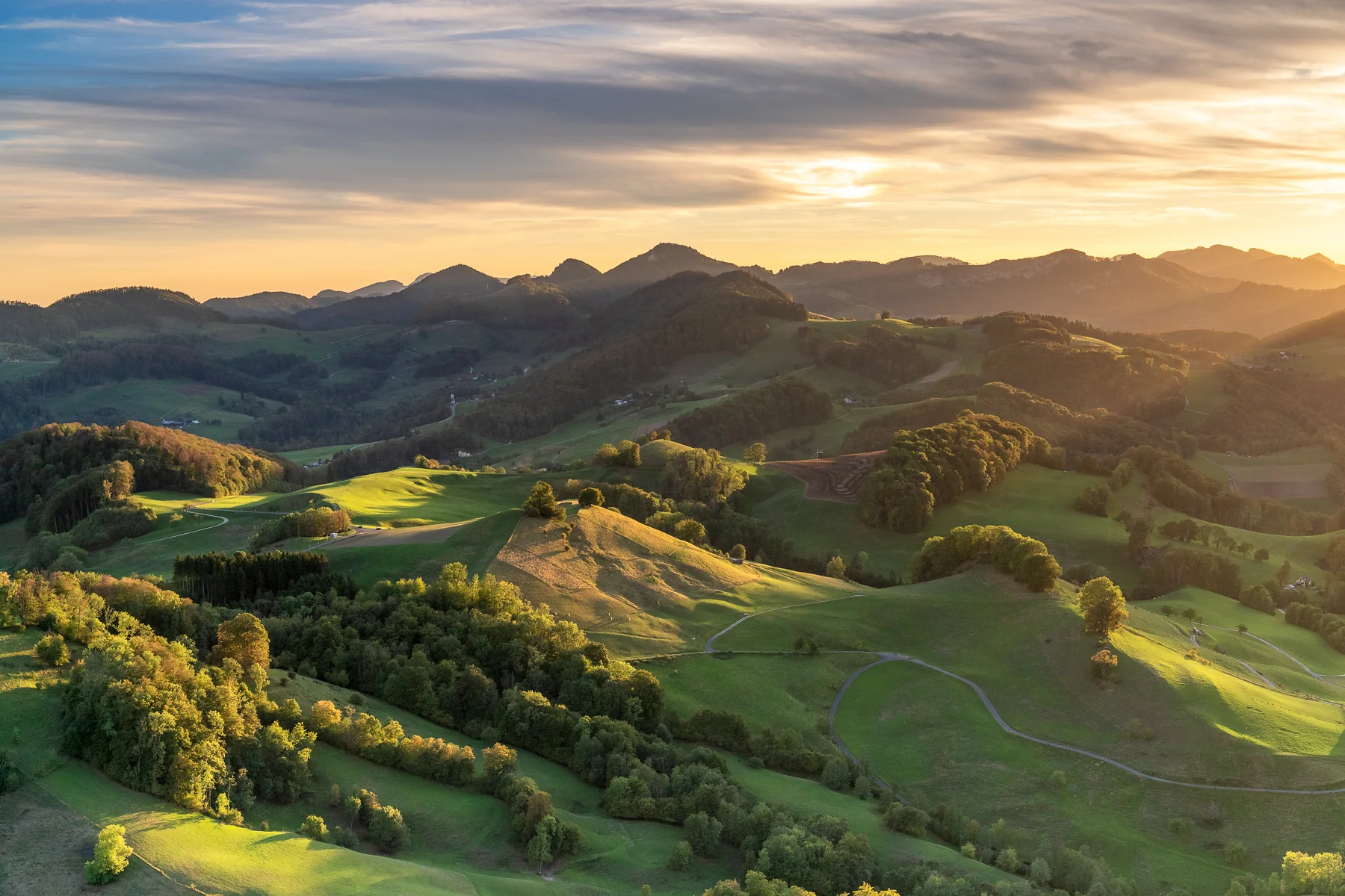 Idyllische Hügellandschaft in Baselland mit grünen Wiesen, Wäldern und Bergen bei goldenem Sonnenuntergang